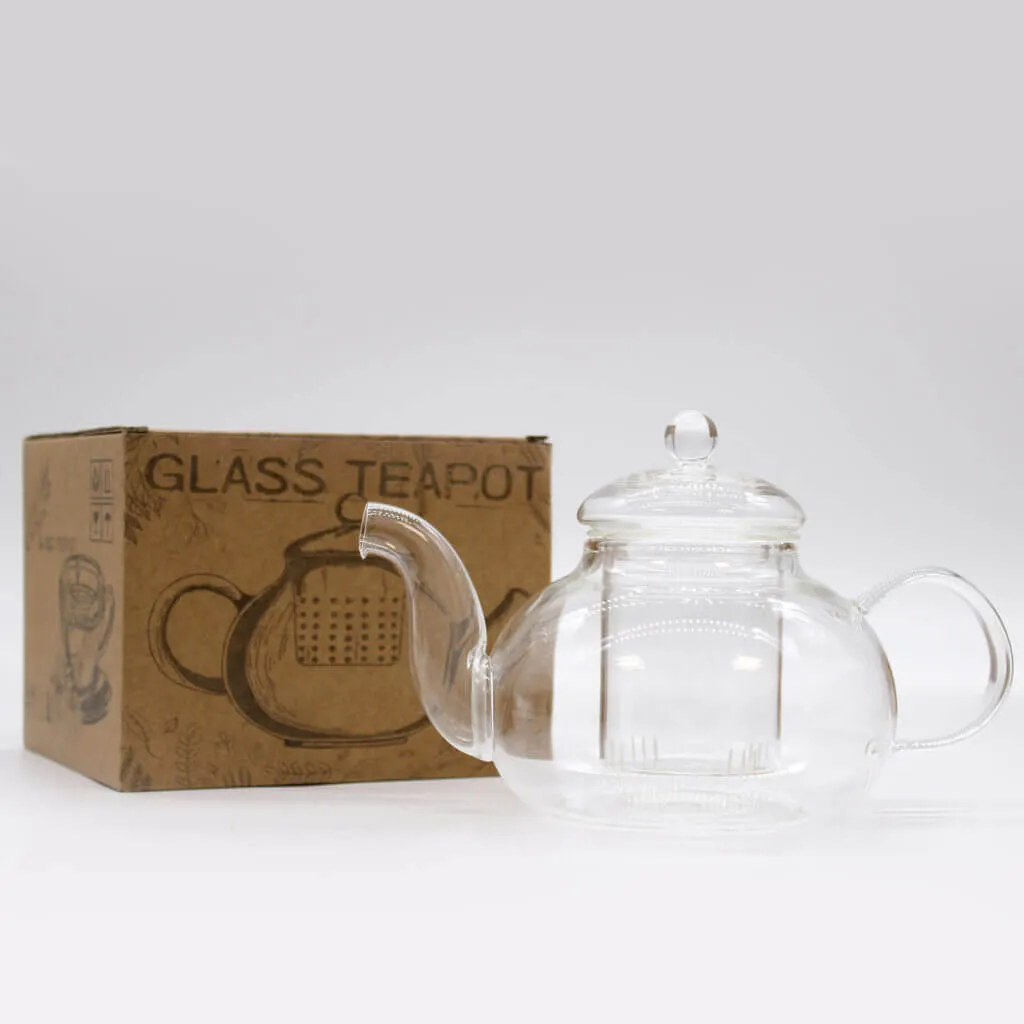 A clear glass teapot with a lid is placed next to a brown cardboard box labeled 