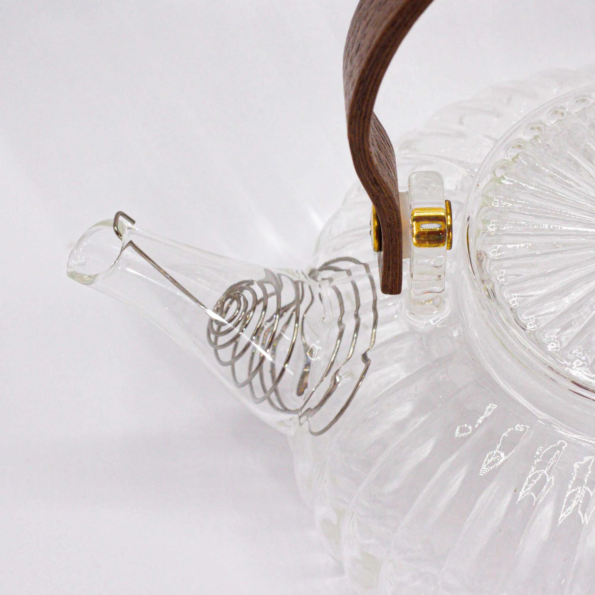 Clear glass teapot with a ribbed pattern, wooden handle, and metal spiral filter at the spout, set against a white background.