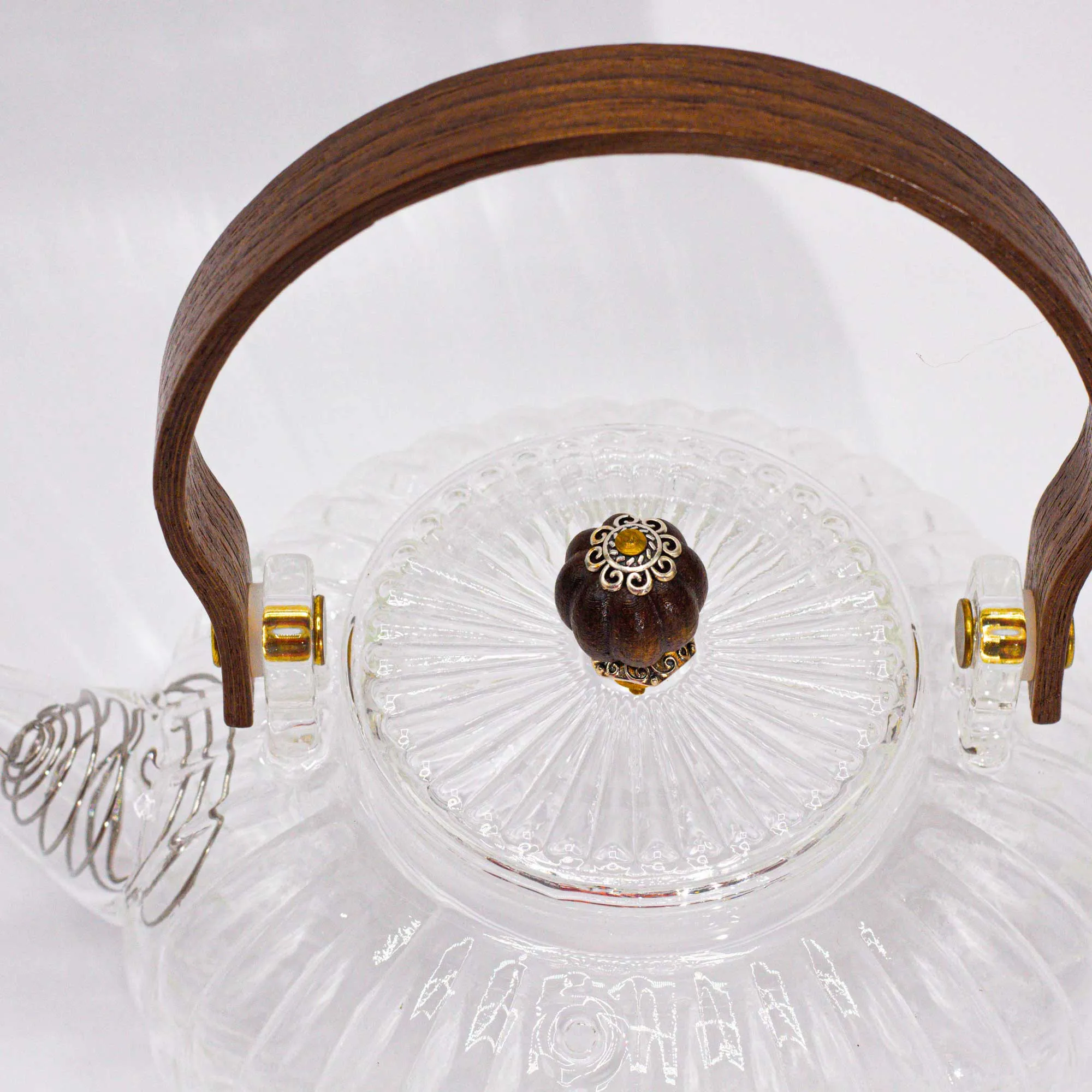 Clear glass teapot with a textured lid, wooden handle, and gold-colored decorative knob, viewed from above.