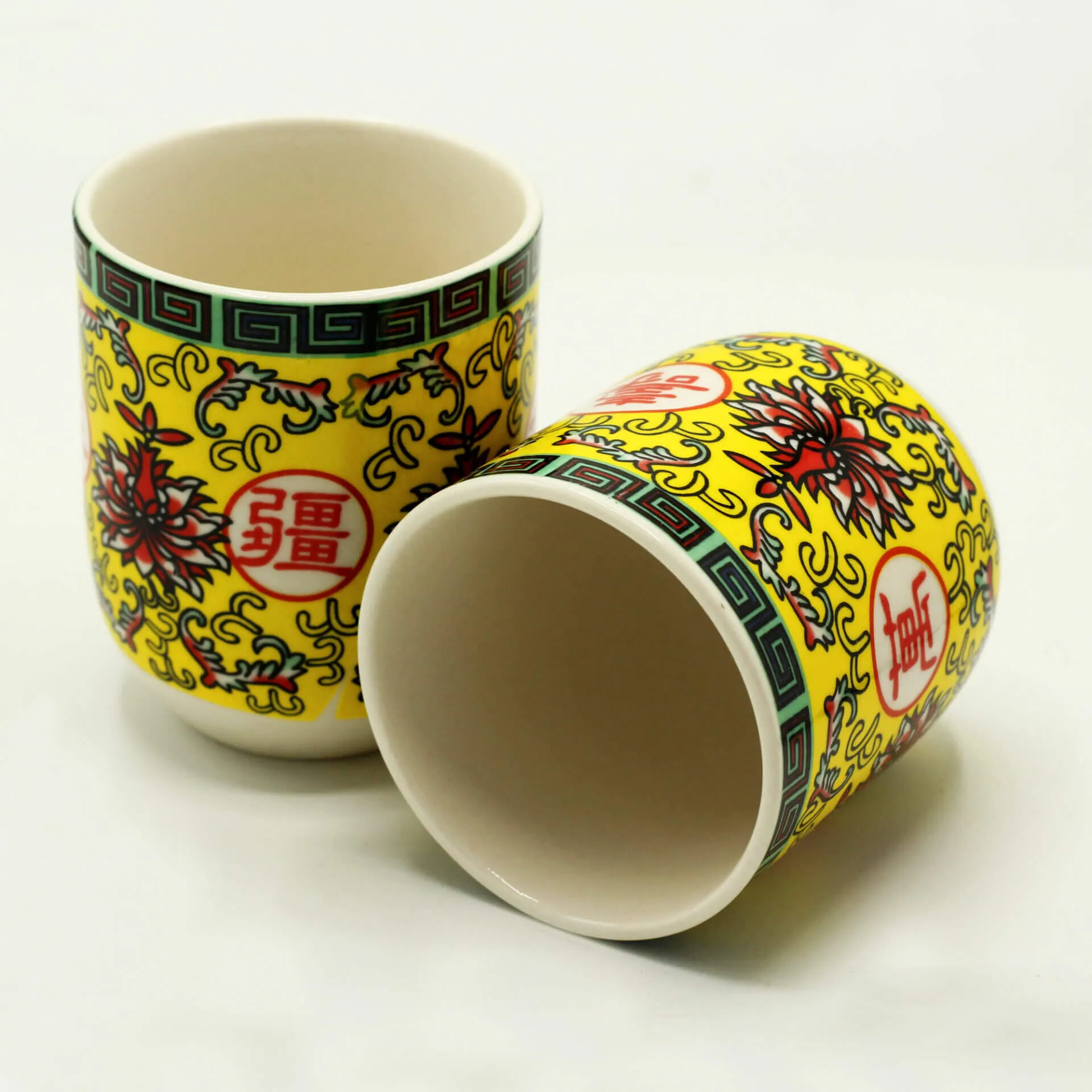 Two ceramic cups with yellow backgrounds, floral patterns, and red Chinese characters, one standing upright and one lying on its side.