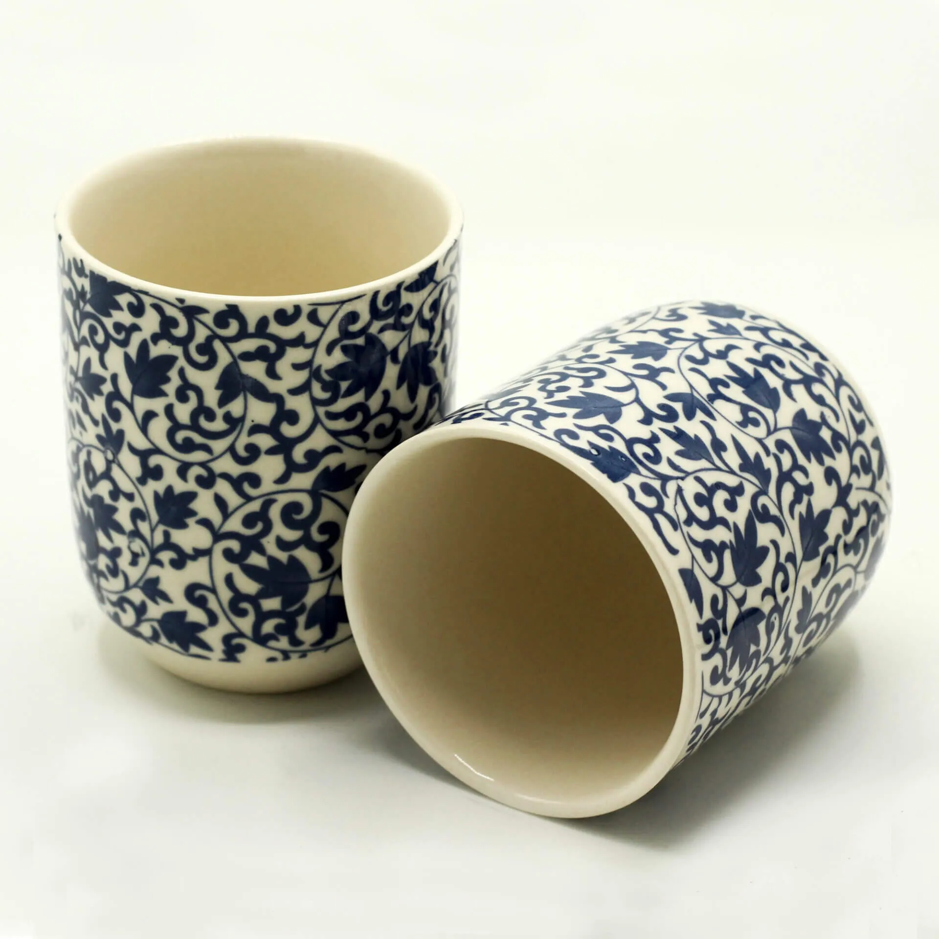 Two ceramic cups with blue floral patterns; one standing upright and the other lying on its side, both on a plain white background.