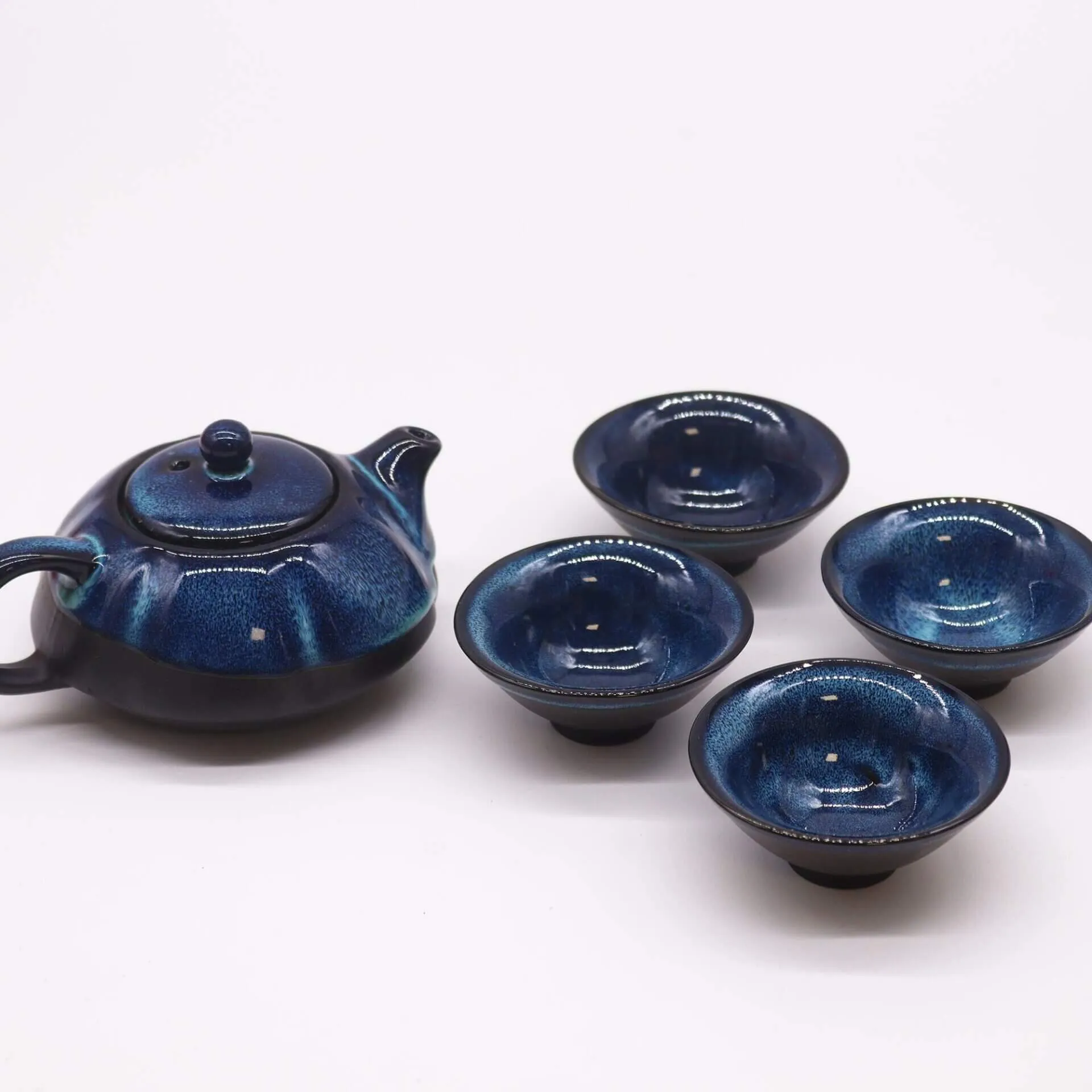 A dark blue ceramic teapot with a matching lid and four matching ceramic teacups arranged on a white background.