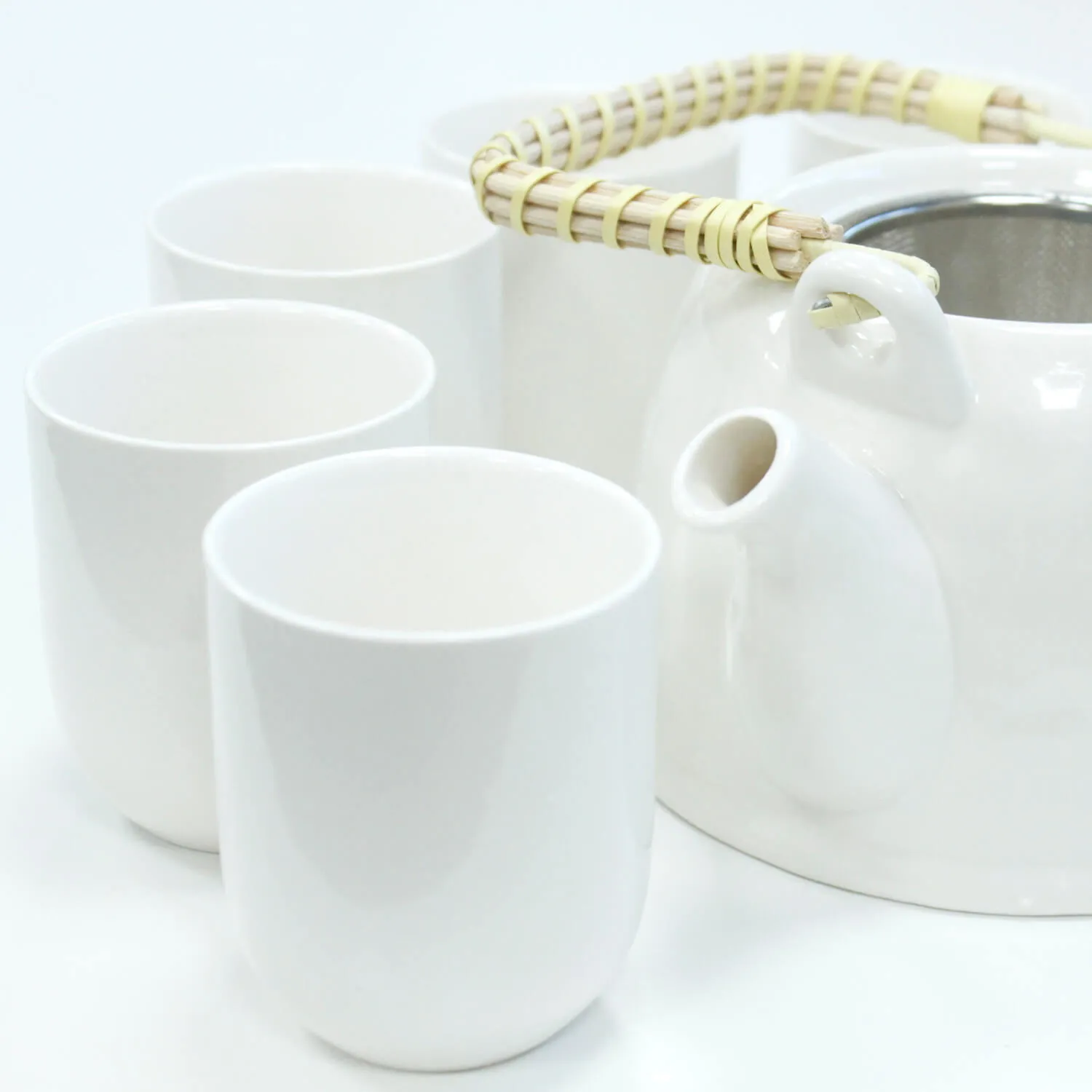 A white ceramic teapot with a woven handle is placed next to four matching white cups on a white surface.