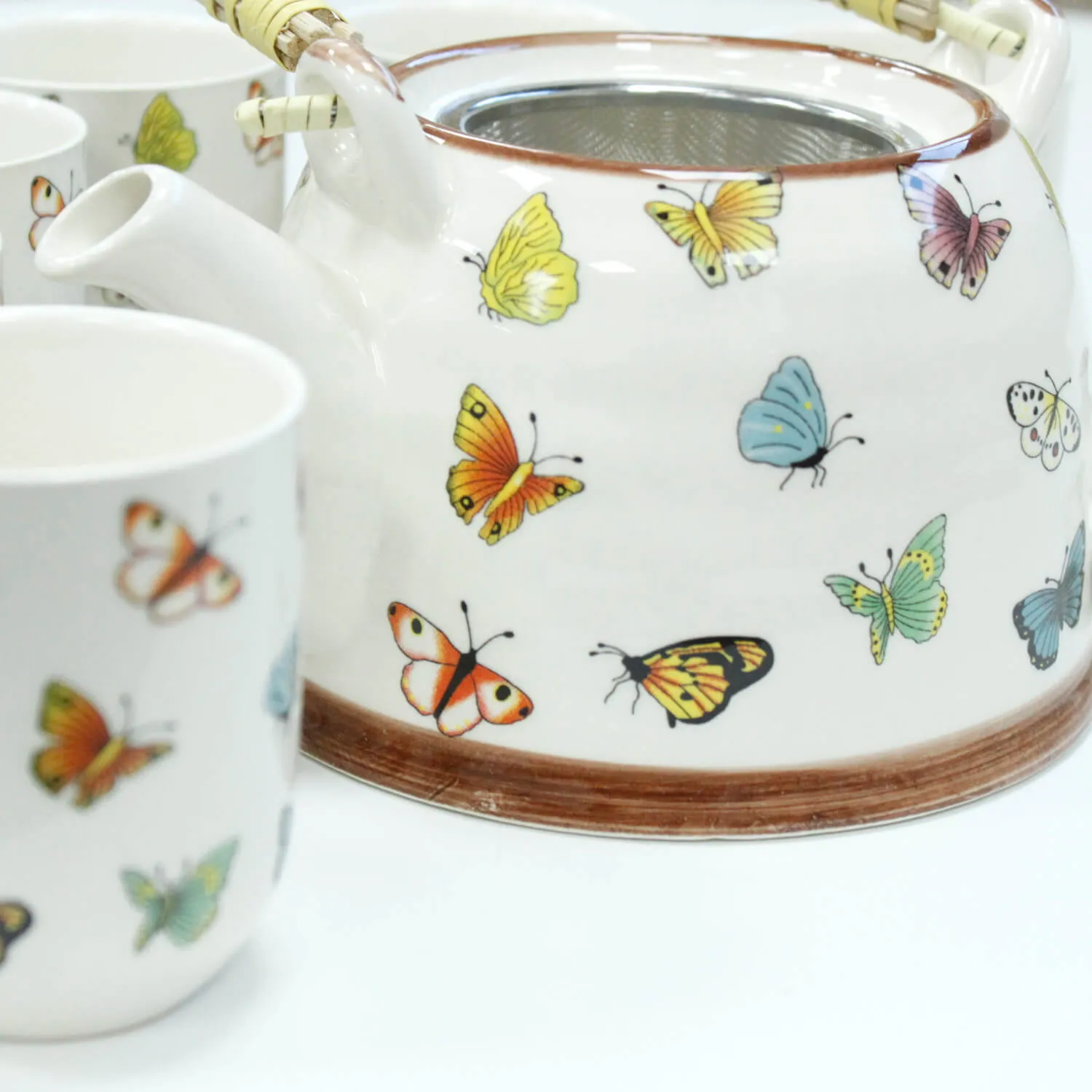 A white teapot and cup decorated with colorful butterfly illustrations on a plain background.