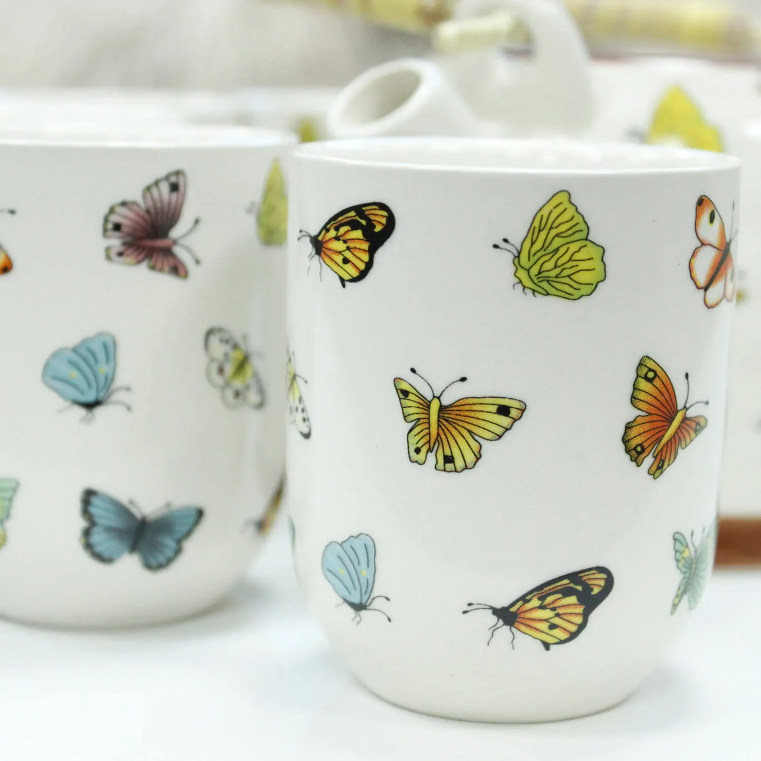White ceramic mugs decorated with colorful butterfly illustrations in various sizes and positions.