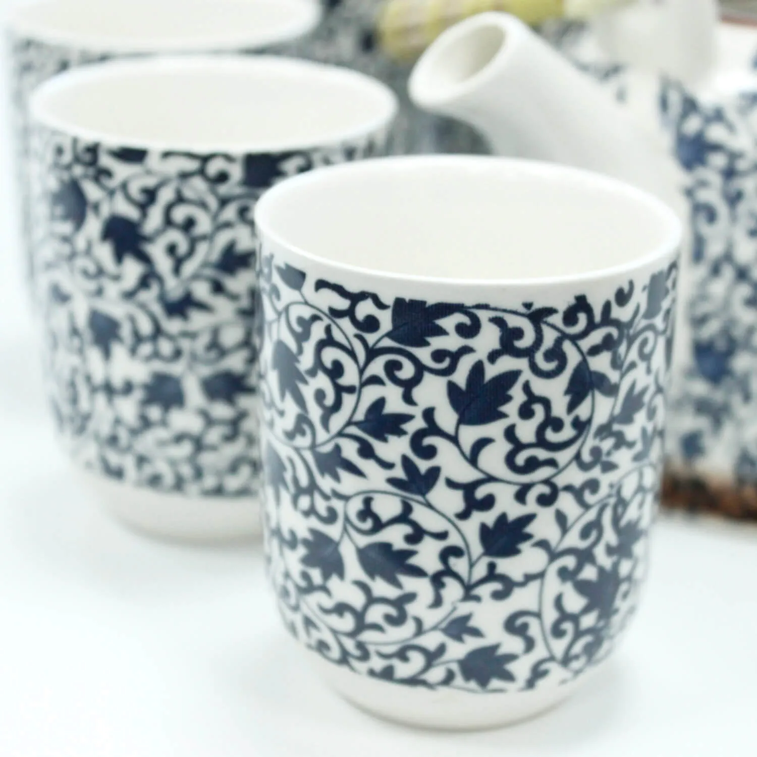 Close-up of white ceramic cups with intricate dark blue floral patterns, accompanied by a matching teapot in the background.