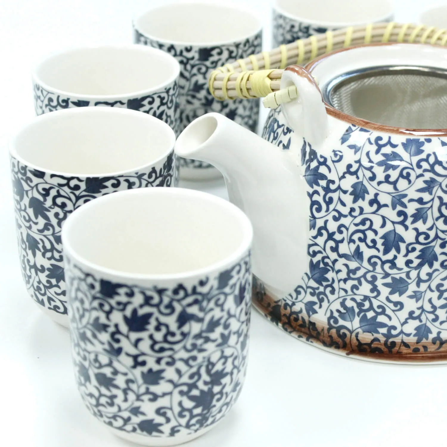 A ceramic teapot with a wicker handle and five matching blue and white patterned cups arranged on a white surface.