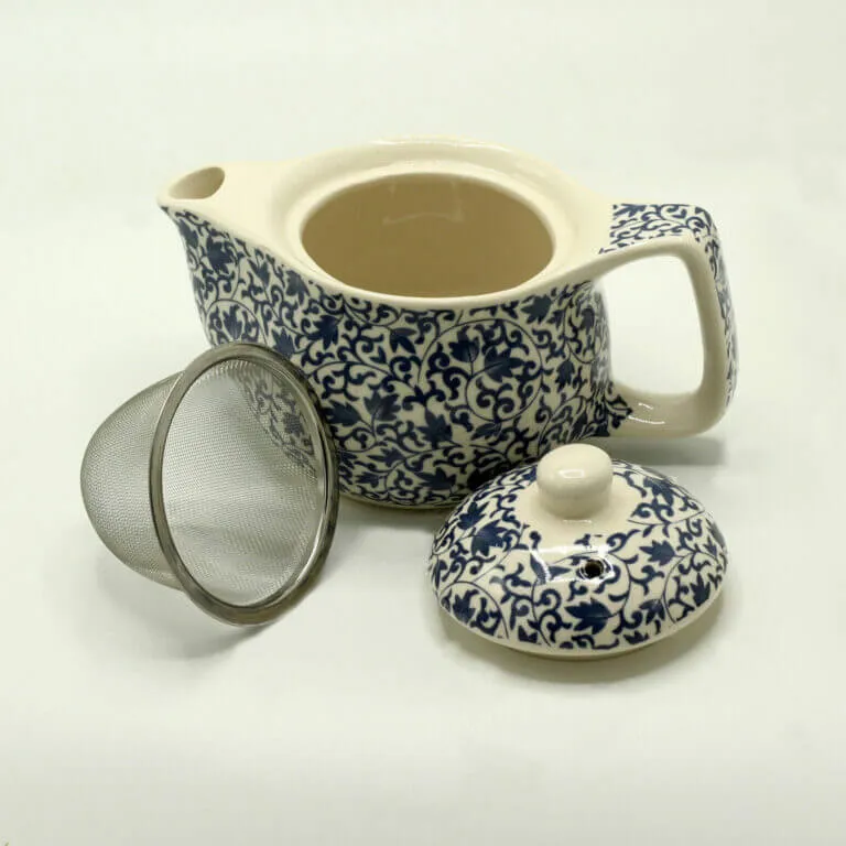 A ceramic teapot with a blue and white floral pattern, shown with its matching lid removed and a metal mesh tea infuser beside it.