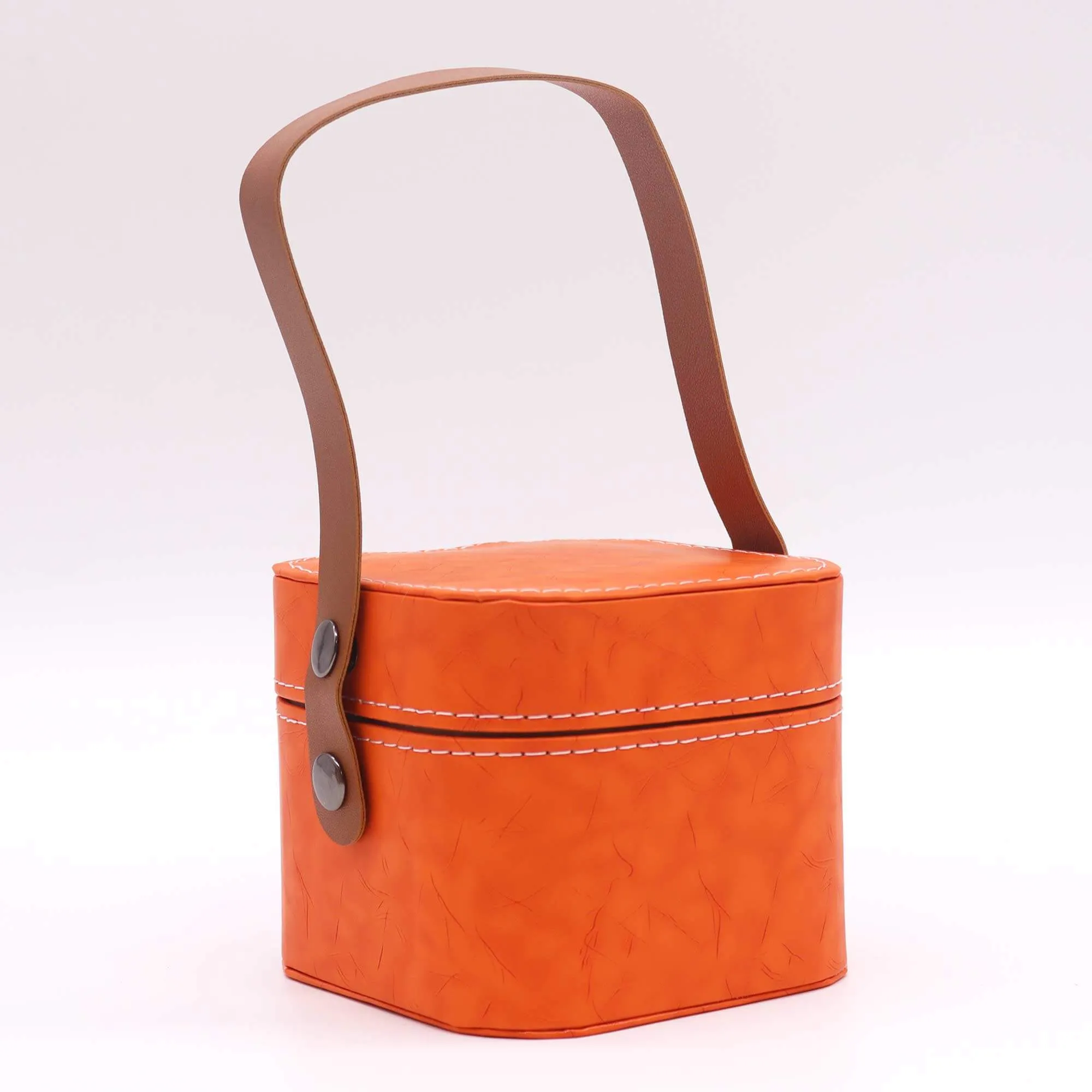 An orange, hexagonal leather container with white stitching and a brown handle attached by two metal studs on each side.