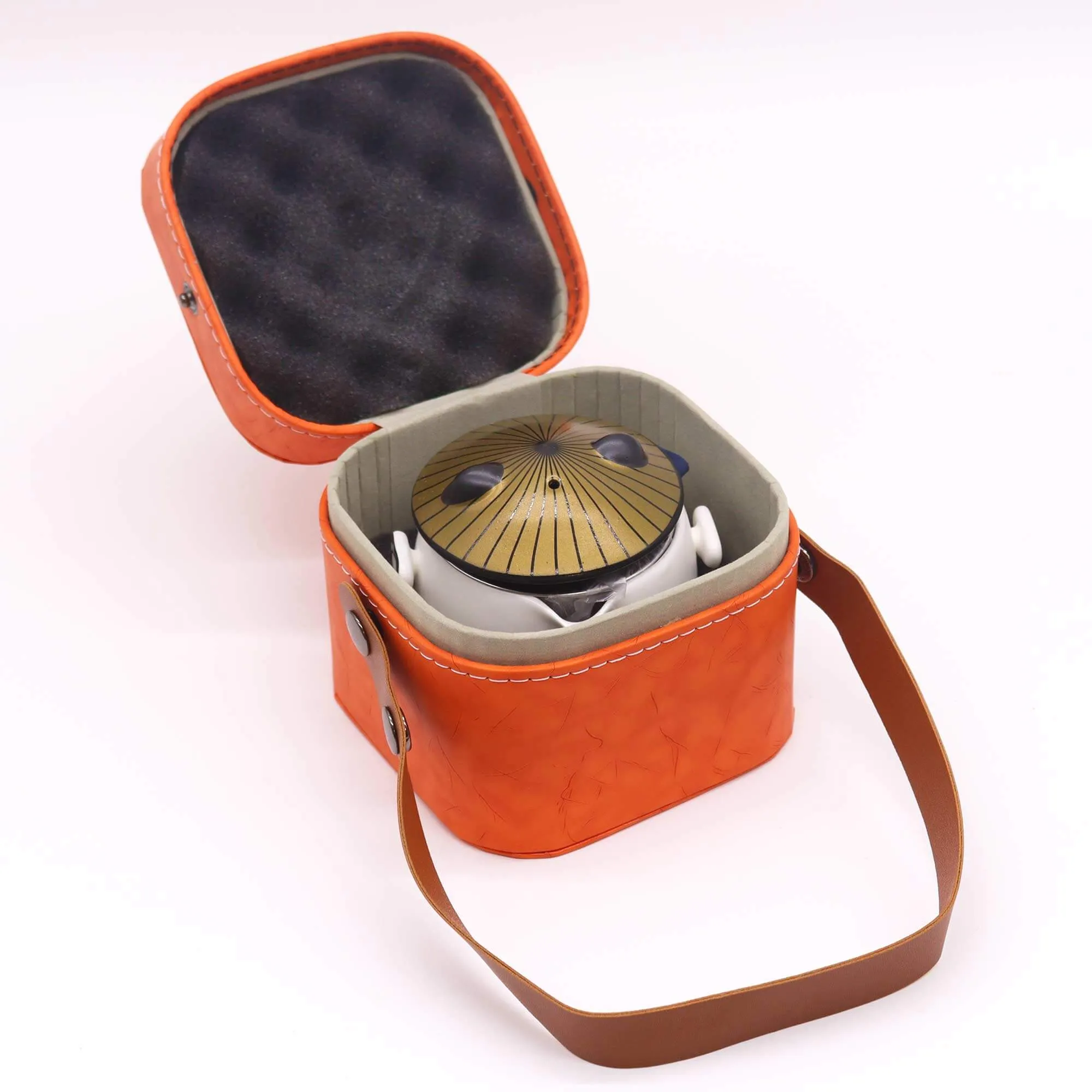 A small steel tongue drum in an orange carrying case with a brown strap and gray interior, shown on a white background.