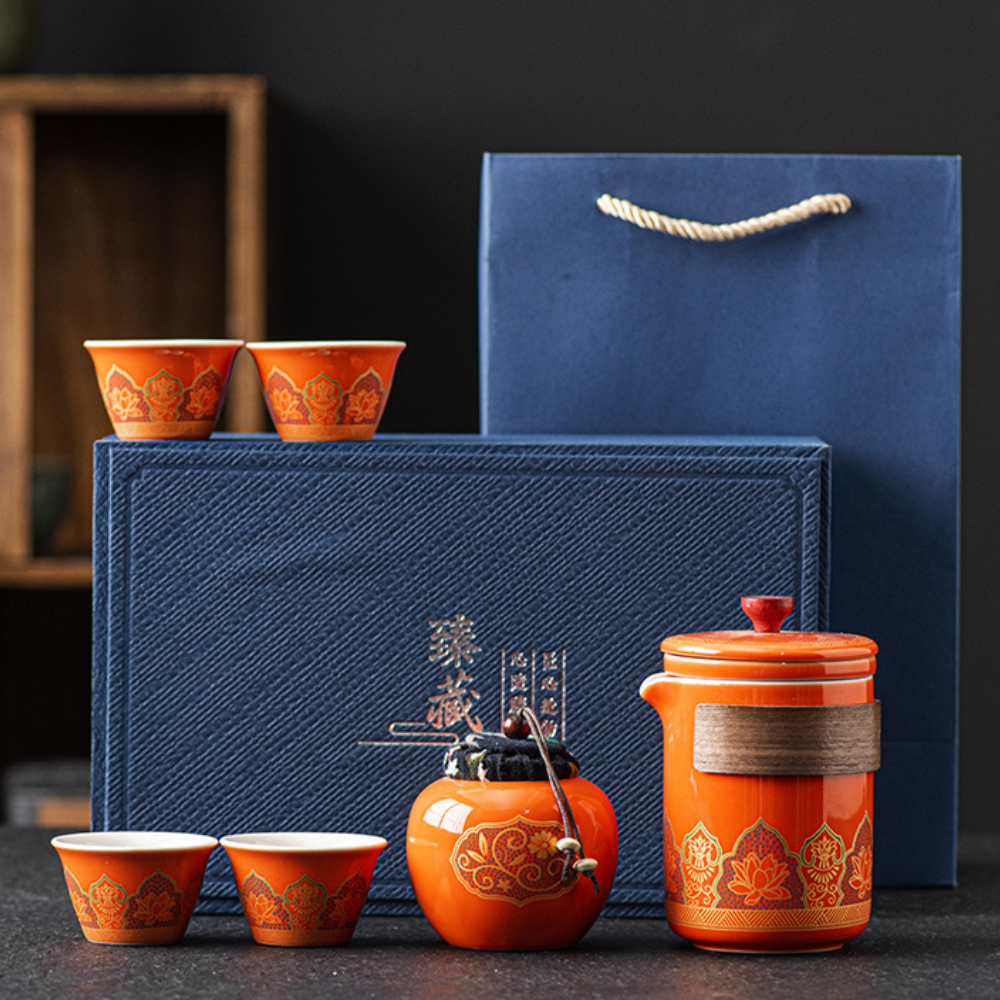 A blue gift box and bag with an orange teapot, four matching teacups, and a small orange container, all decorated with gold patterns.