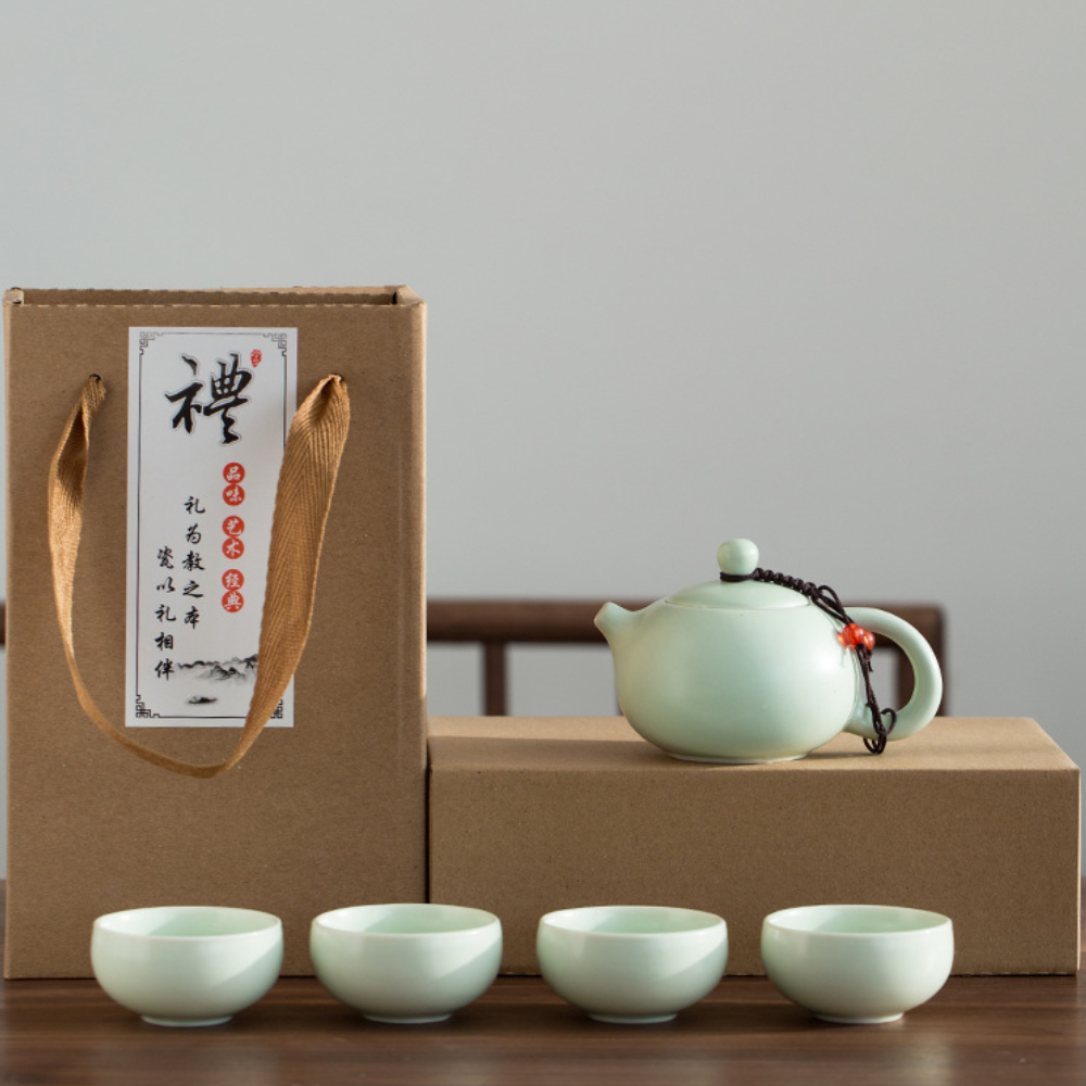 A ceramic teapot with four matching cups is displayed in front of two cardboard boxes, one with a rope handle and a label featuring Chinese calligraphy.