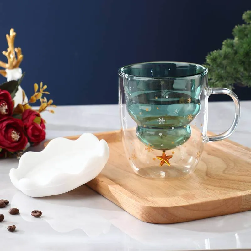 Glass mug with a green top and gold star design on a wooden tray. White dish and decorative flowers are nearby.